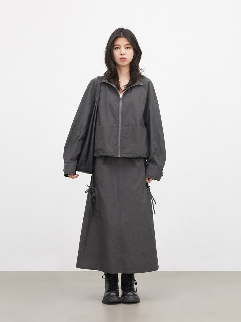 Model wearing a dark gray zip-up jacket with matching long skirt and black boots