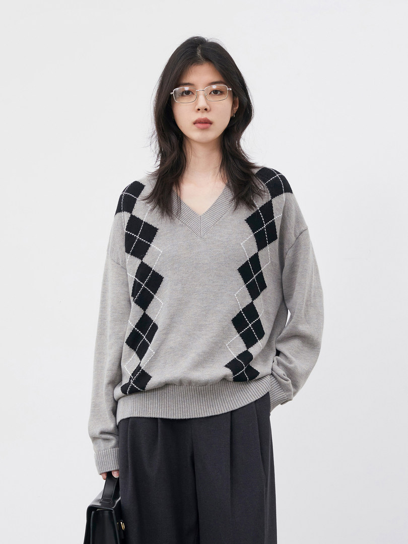 Model wearing a gray argyle V-neck sweater with black skirt