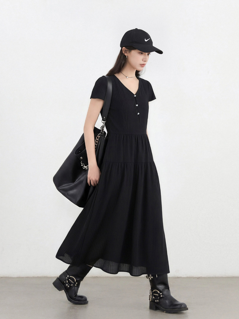Model wearing a black short-sleeve midi dress with black boots, cap, and shoulder bag
