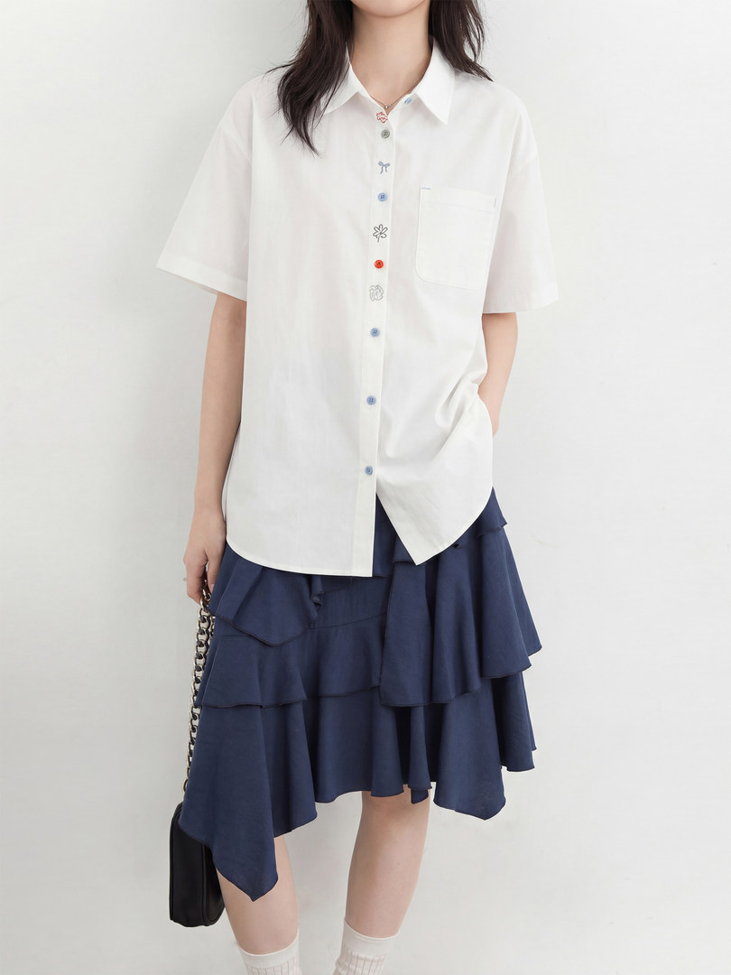 Model wearing a white short-sleeve button-up shirt with a navy layered skirt