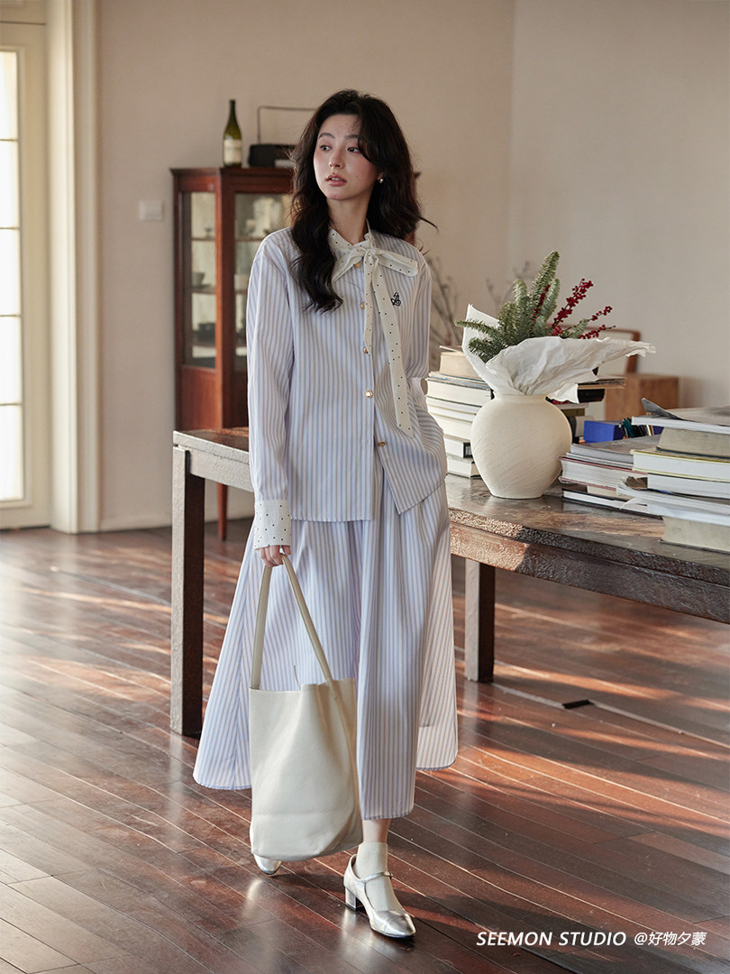 Model wearing a light striped matching blouse and skirt set with a tote bag
