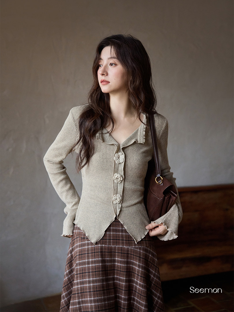 Model wearing a beige ribbed long-sleeve top with floral buttons and a plaid skirt