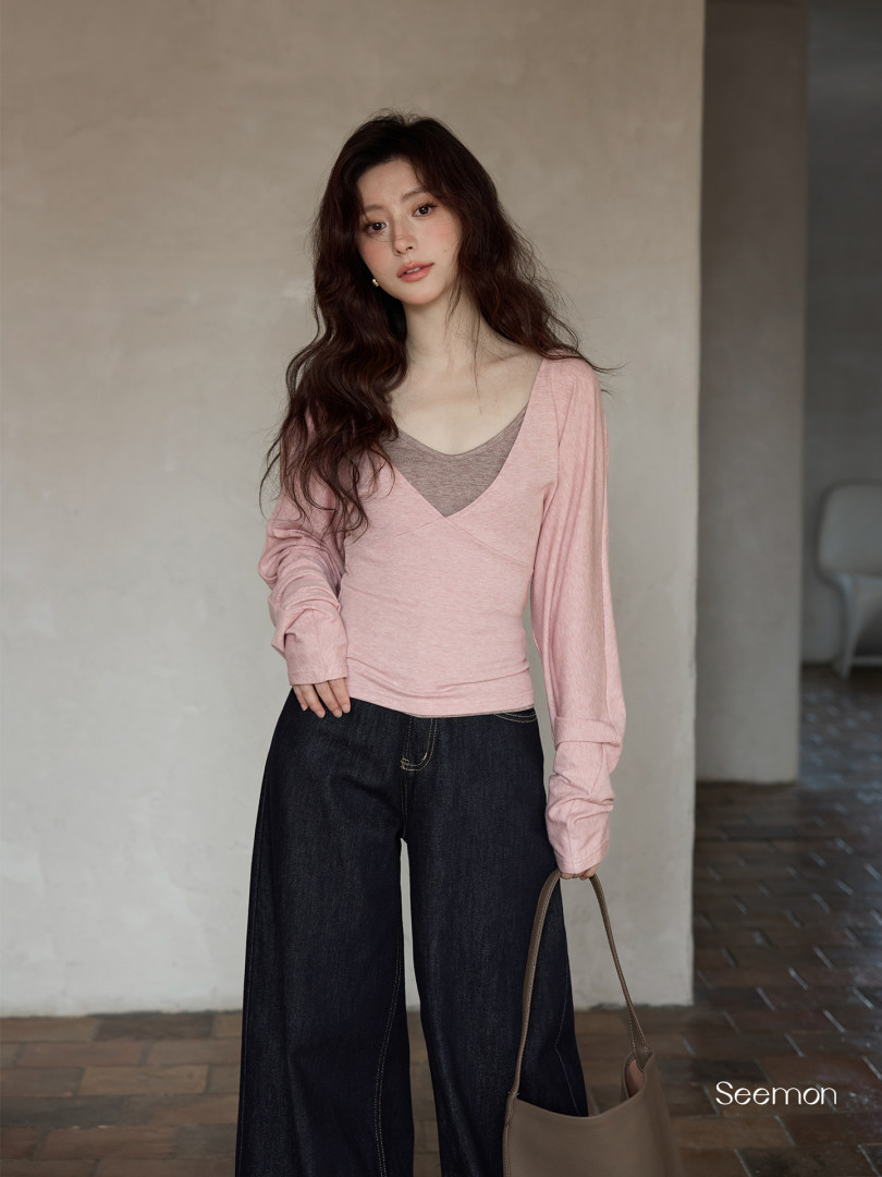 Model wearing a pink long-sleeve layered top with dark wide-leg jeans and a handbag