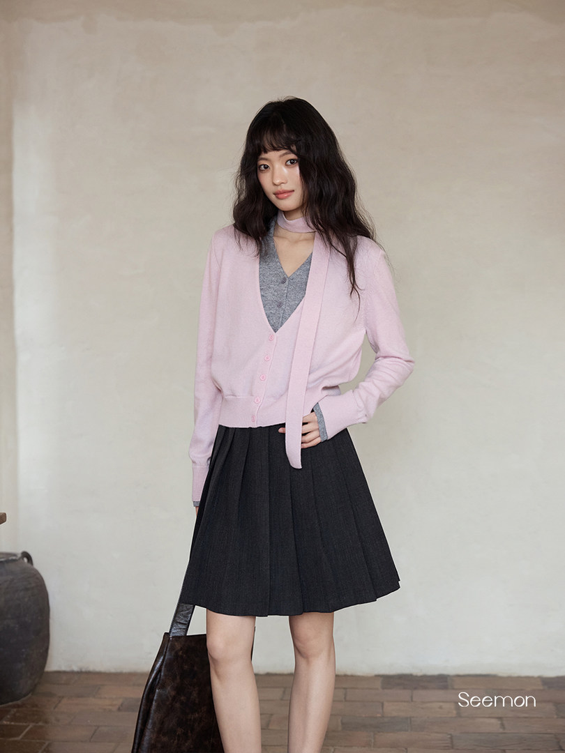 Woman modeling a light pink cardigan with a black pleated skirt