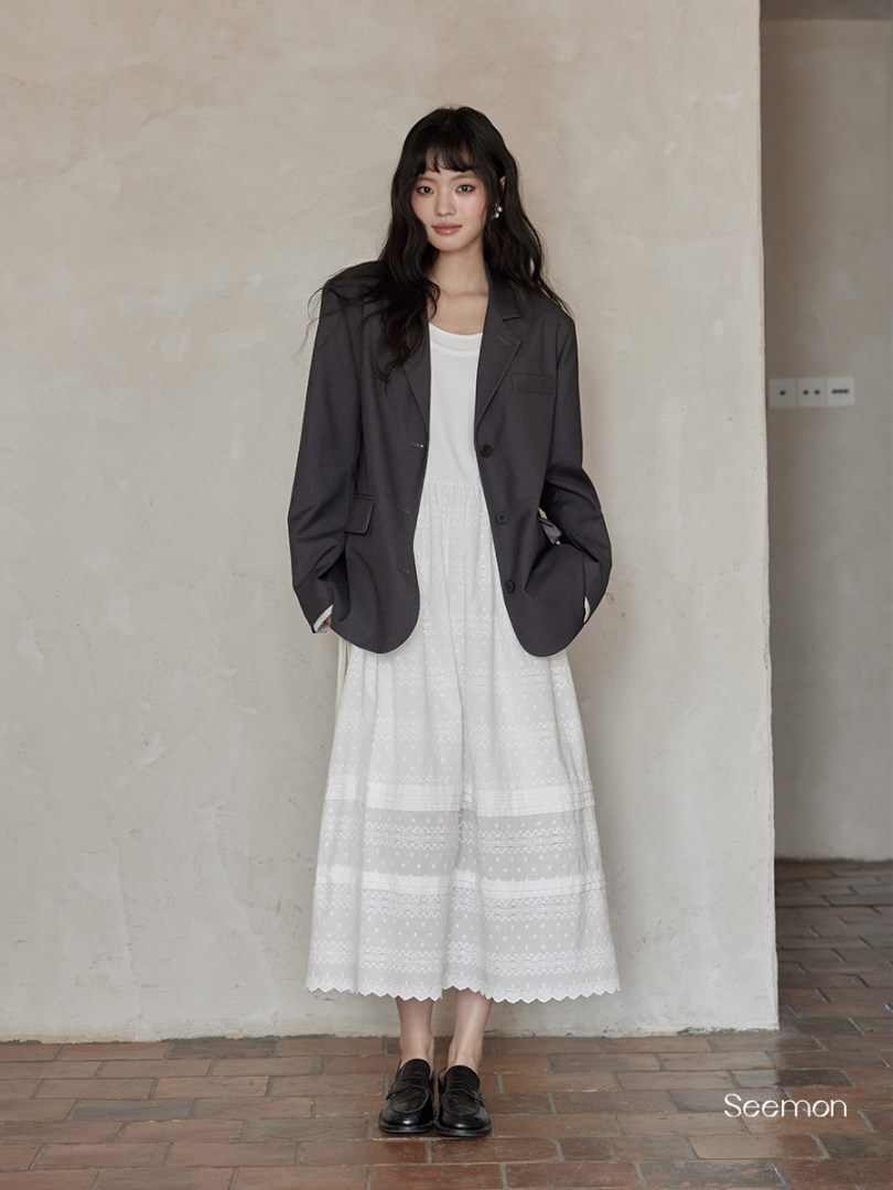 Woman wearing a dark blazer over a white midi dress with black loafers