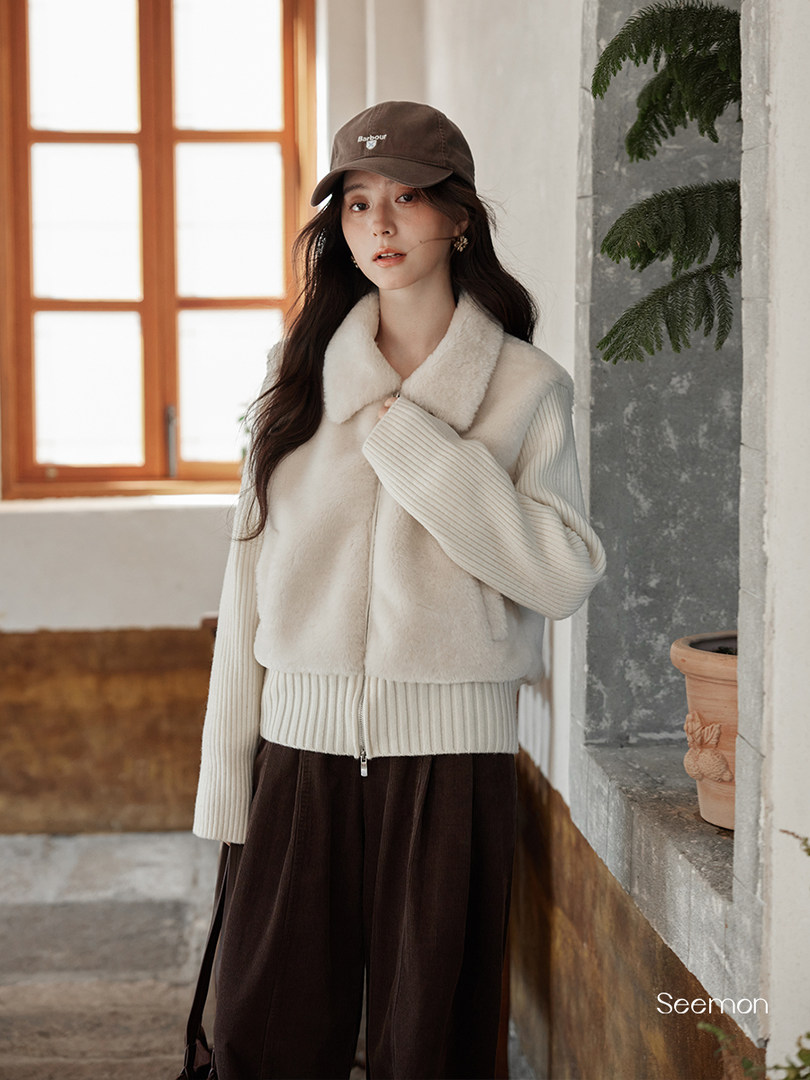 Woman wearing a cream fleece vest and ribbed sweater with a brown cap
