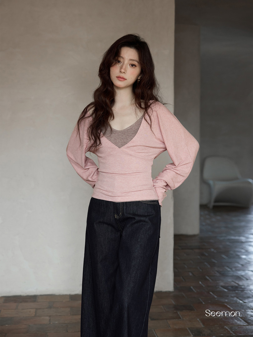 Model wearing a pink long-sleeve wrap top with a layered neckline and dark jeans