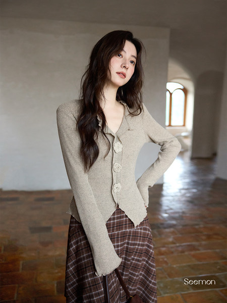 Model wearing a beige knit cardigan with a plaid skirt