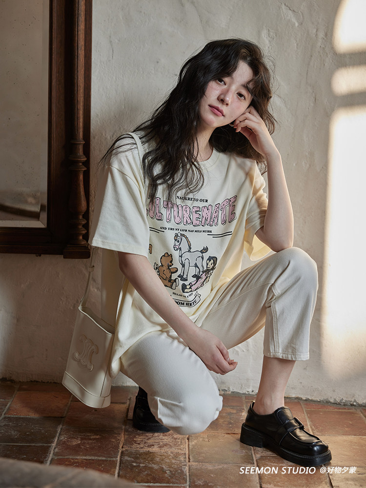 Model wearing a cream graphic oversized T-shirt with white cropped pants and black loafers
