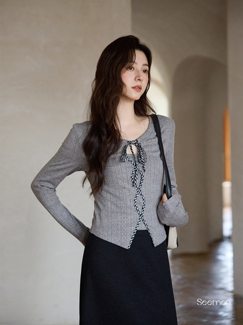 Woman wearing a gray long-sleeve knit top with a tie front and black skirt
