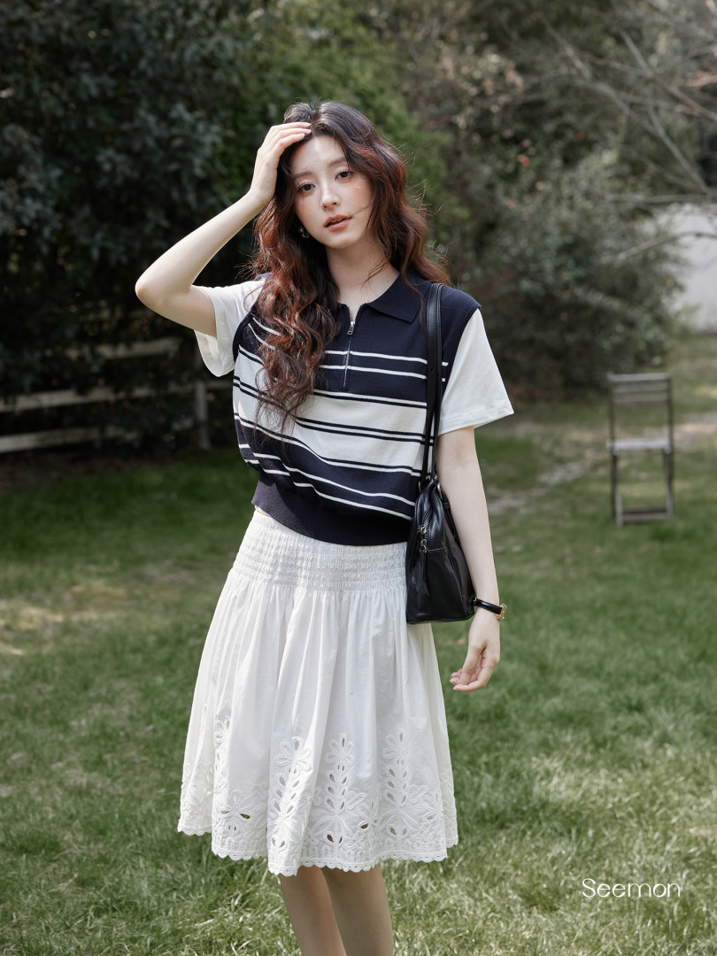 Woman modeling a striped polo top with a white lace skirt and black shoulder bag outdoors