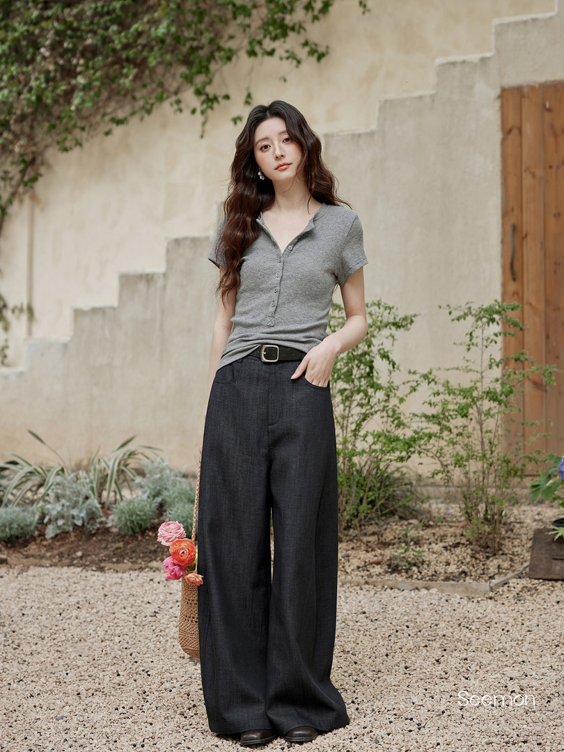 Model wearing a gray short-sleeve knit top with wide-leg dark pants and a woven bag