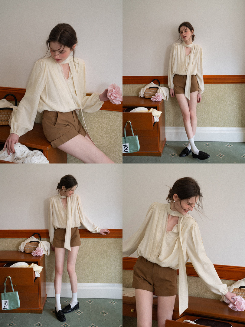 Model wearing a cream long-sleeve blouse with brown shorts in a styled indoor photoshoot
