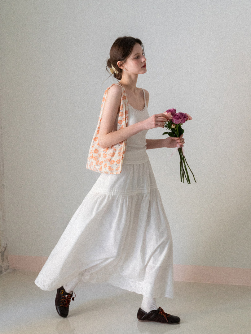 Model wearing a white flowing skirt and camisole with a floral tote bag