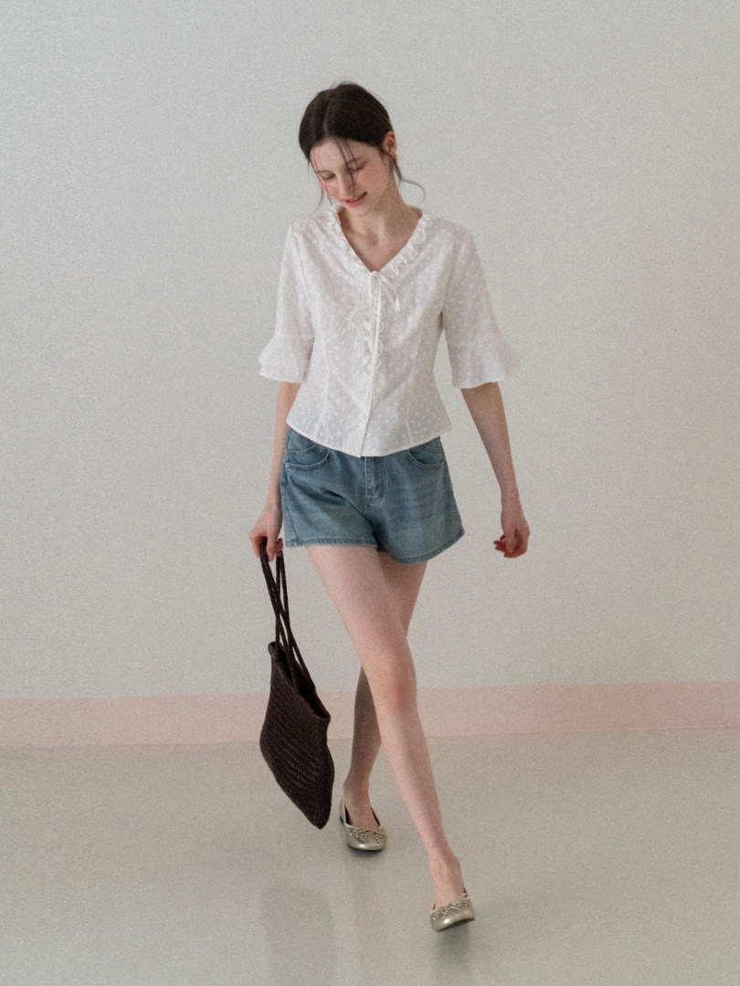 Woman wearing a white blouse and denim shorts with a woven handbag