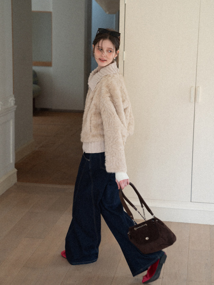 Woman modeling a beige faux fur jacket with wide-leg dark jeans and a handbag indoors