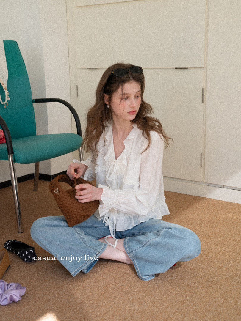 Woman wearing a white ruffled blouse and light blue jeans while holding a brown woven handbag