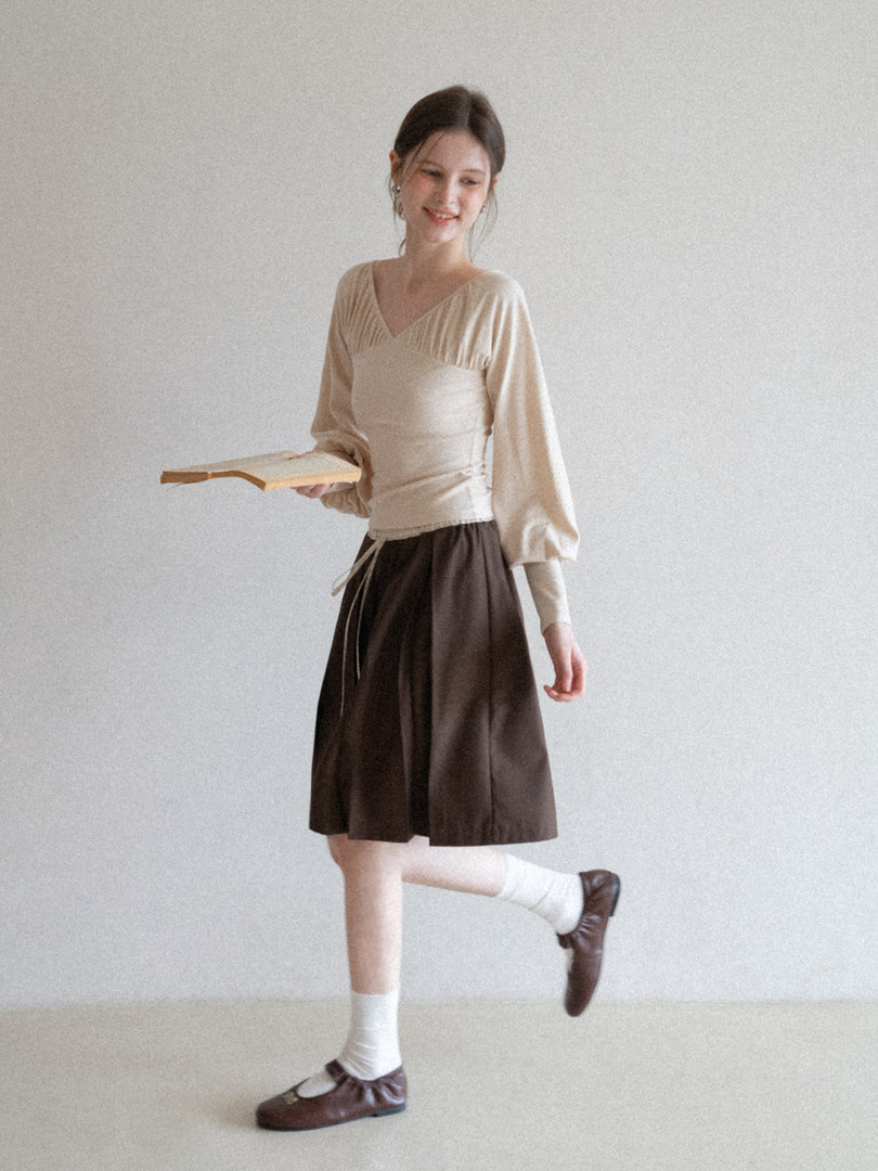 Model wearing a beige long-sleeve top with a brown skirt and brown flats