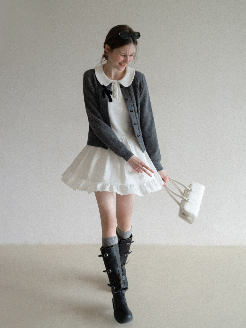 Model wearing a gray cardigan over a white dress with black boots