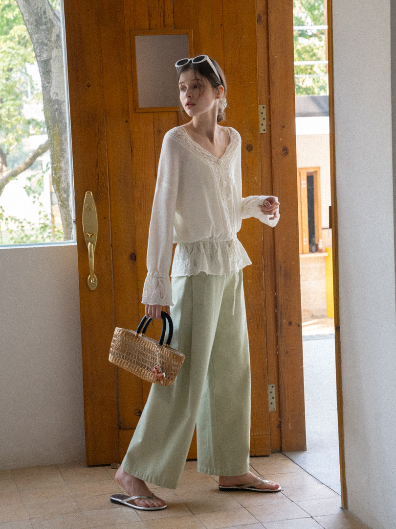 Woman wearing a white blouse, mint wide-leg pants, and holding a woven handbag
