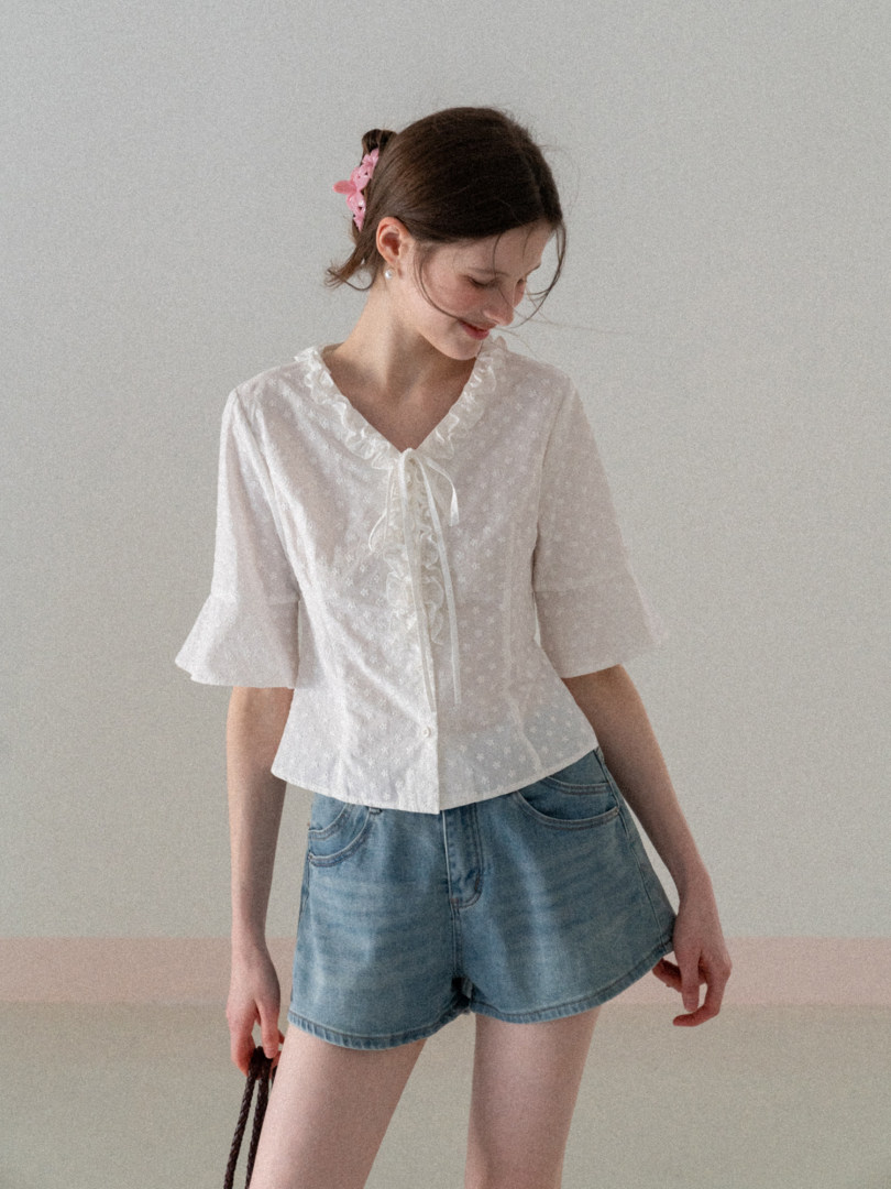Model wearing a white ruffled blouse with light denim shorts