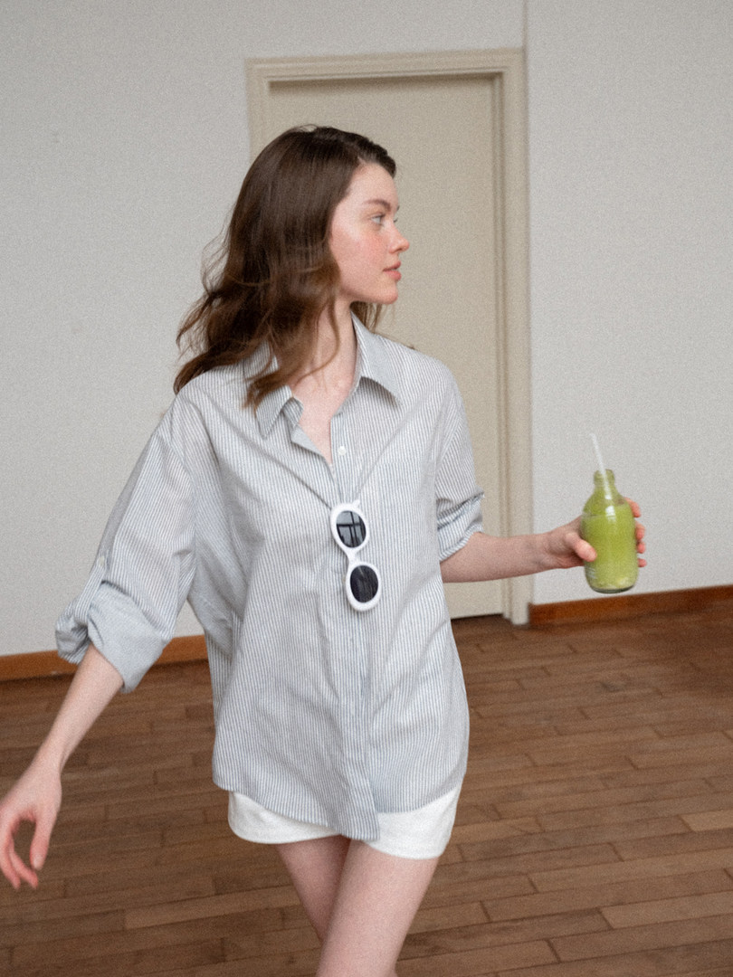 Model wearing a light striped button-up shirt with white shorts while holding a green drink