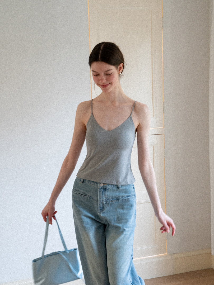 Woman wearing a gray spaghetti-strap tank top with light blue jeans