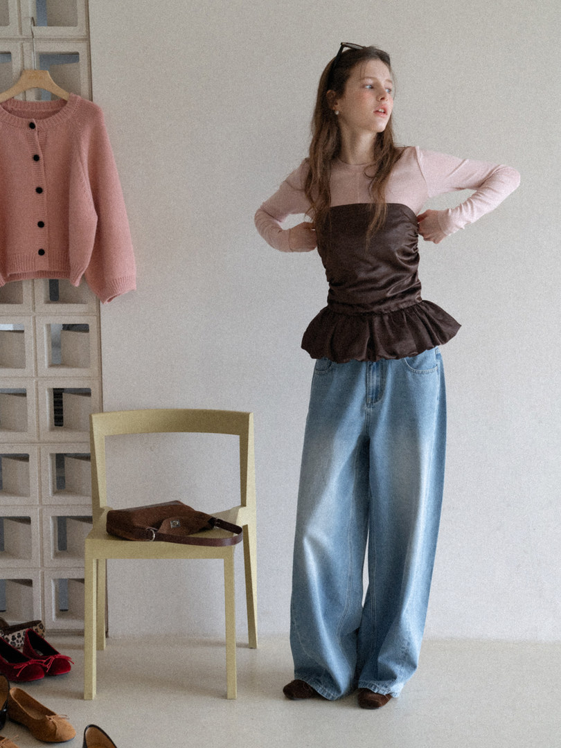 Model wearing a brown strapless peplum top with pink long sleeves and wide-leg blue jeans