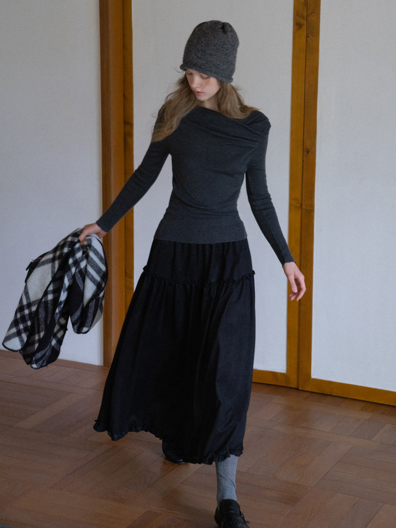 Woman wearing a black long-sleeve top and flowing black skirt with a gray beanie and plaid scarf