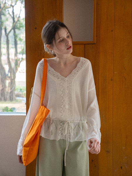 Woman wearing a white lace-trimmed long-sleeve blouse with light green pants and an orange shoulder bag