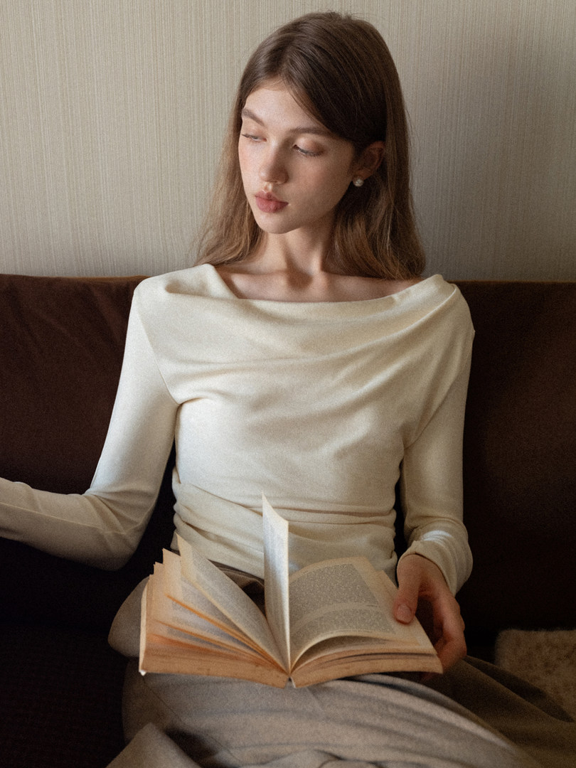 Woman wearing a cream off-shoulder long-sleeve top while holding an open book