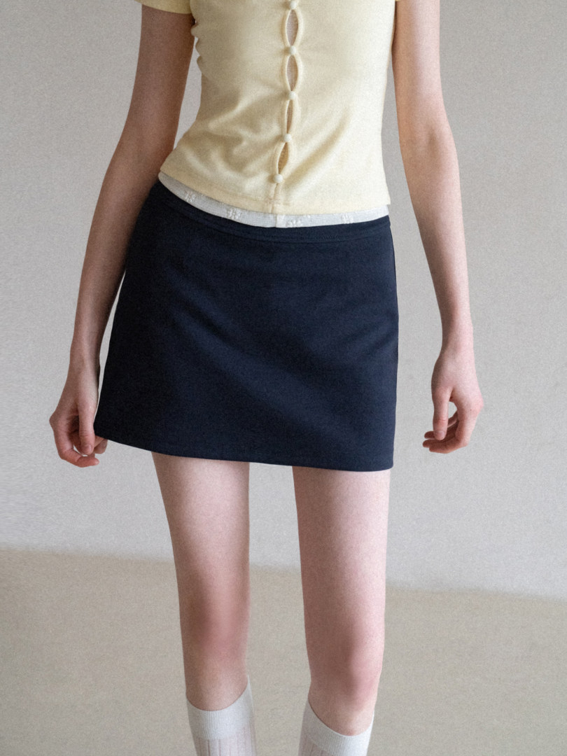 Model wearing a pale yellow sleeveless top with button details and a black mini skirt