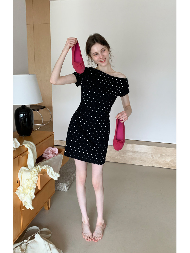 Model wearing a black polka dot off-shoulder dress and holding pink flats