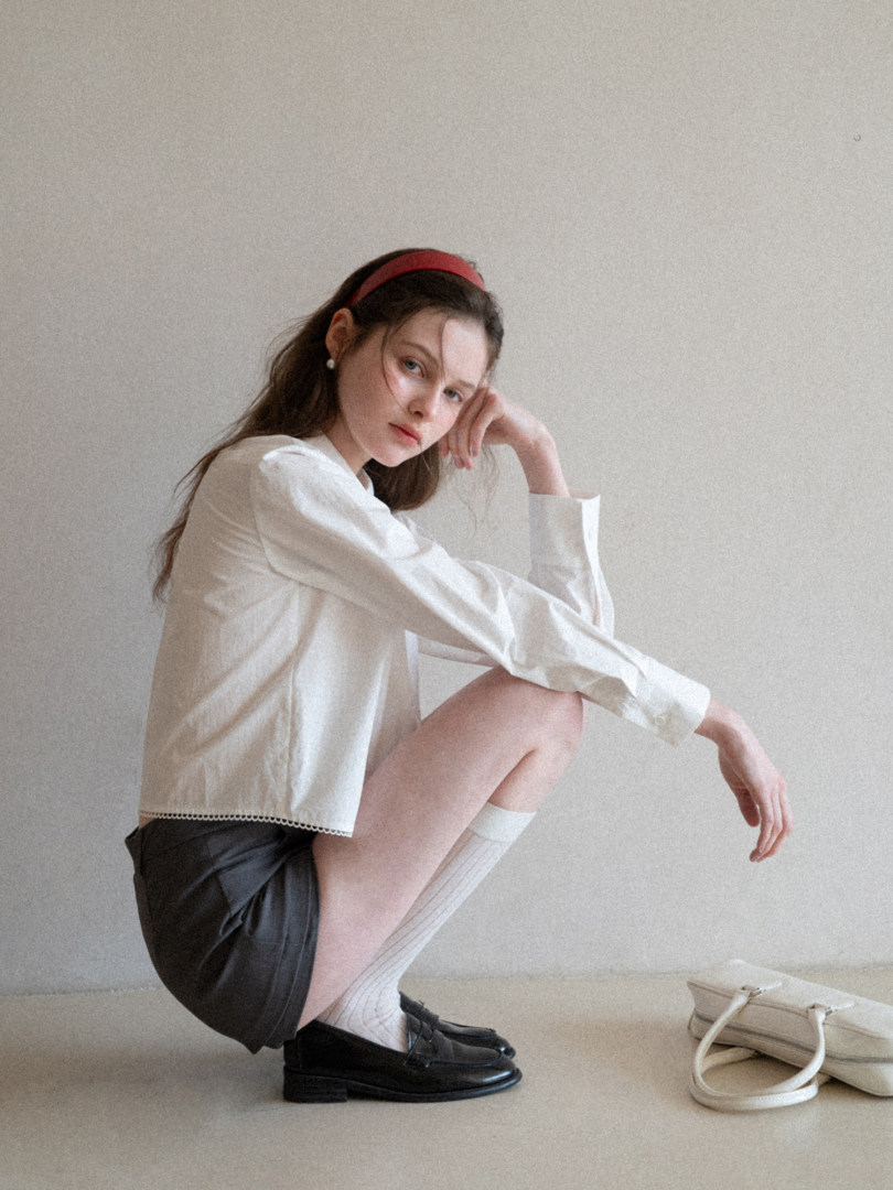 Model wearing a white blouse with black shorts, socks, loafers, and a headband