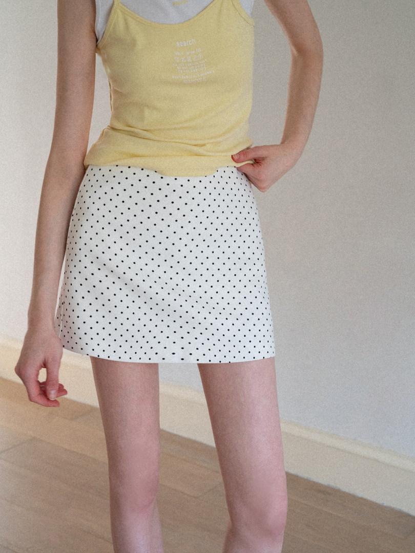 Model wearing a yellow tank top and white polka dot mini skirt
