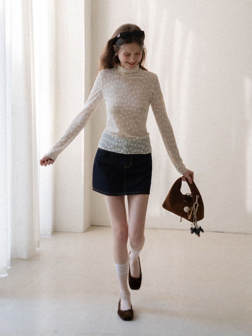 Model wearing a sheer floral long-sleeve top with a denim mini skirt and brown handbag