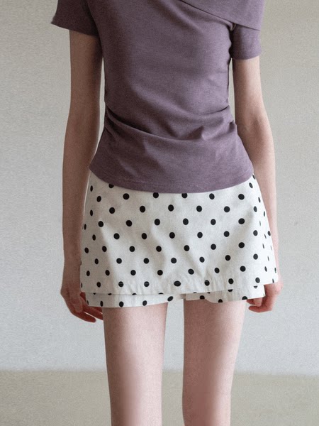 Model wearing a purple fitted top and white polka dot mini skirt
