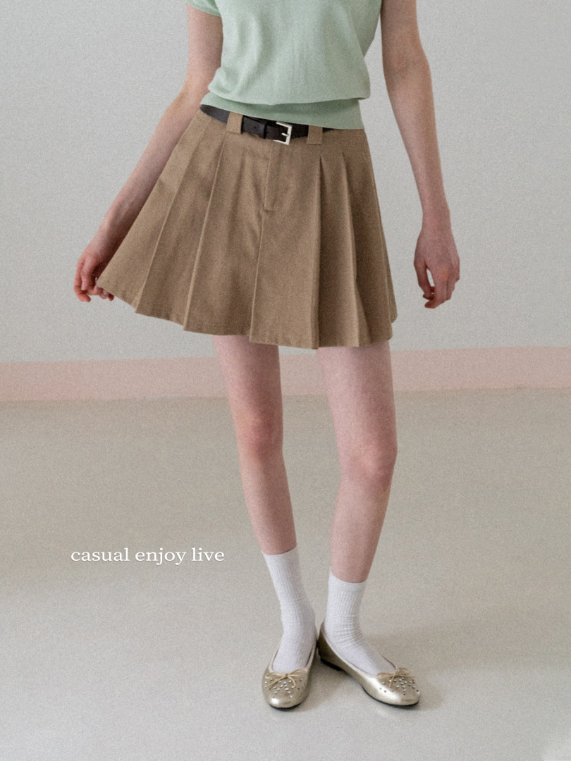 Model wearing a tan pleated skirt with a black belt