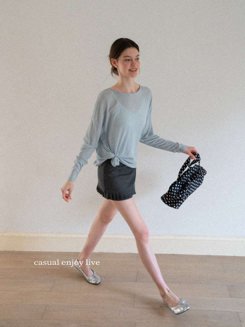 Woman wearing a light blue long-sleeve top and dark shorts, holding a polka dot bag