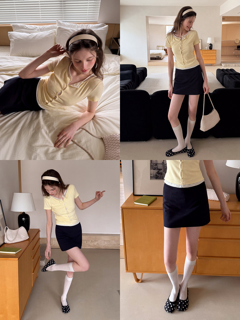 Model wearing a pale yellow short-sleeve top with a black mini skirt in a bedroom setting