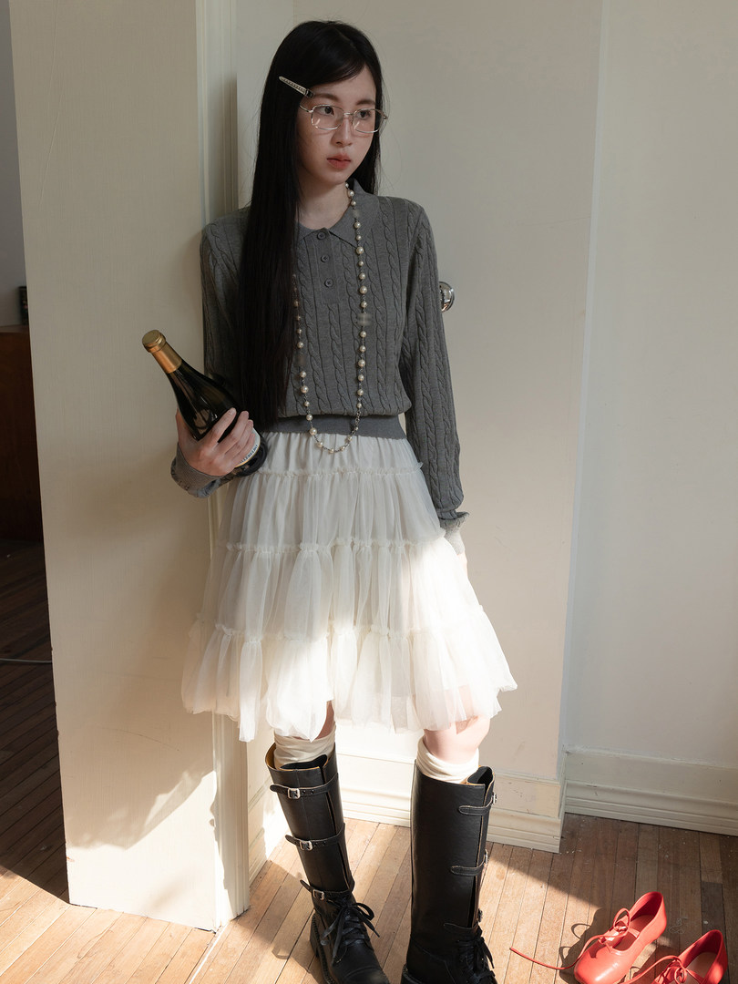 Model wearing a gray cable-knit top, white tiered skirt, and black knee-high boots