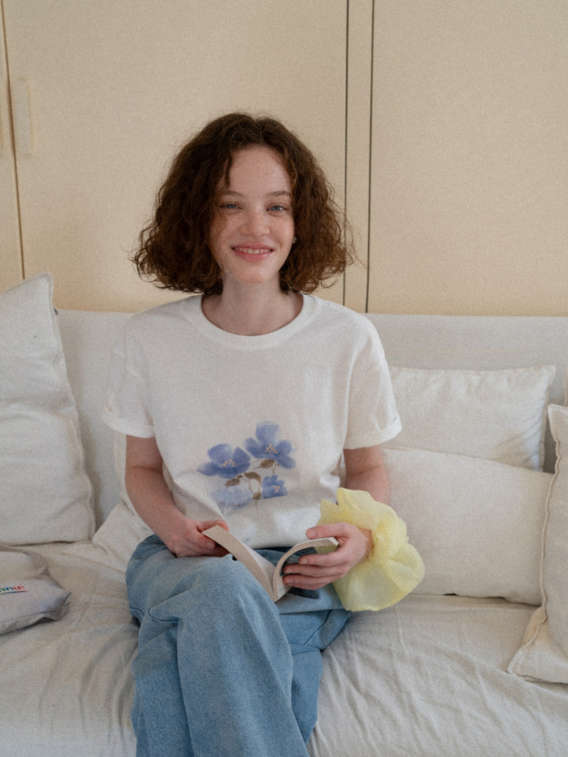 Woman wearing a white floral graphic t-shirt and blue jeans while sitting on a couch