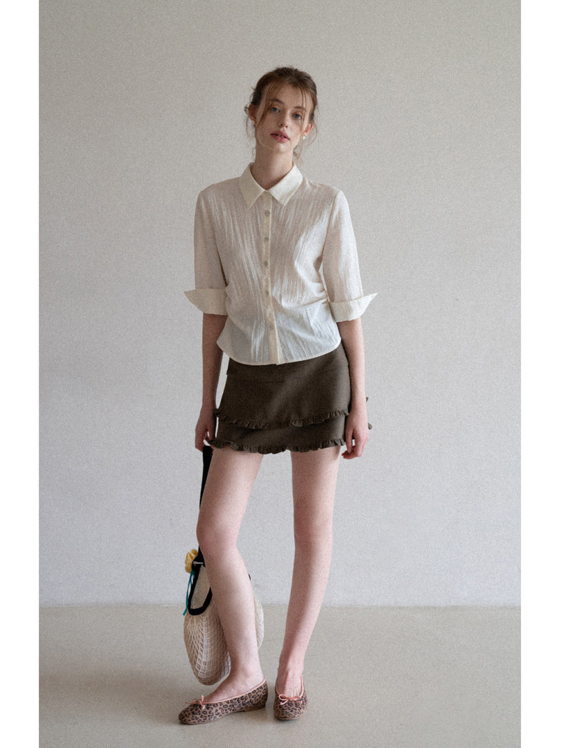 Model wearing a white button-up blouse with an olive mini skirt and leopard flats.