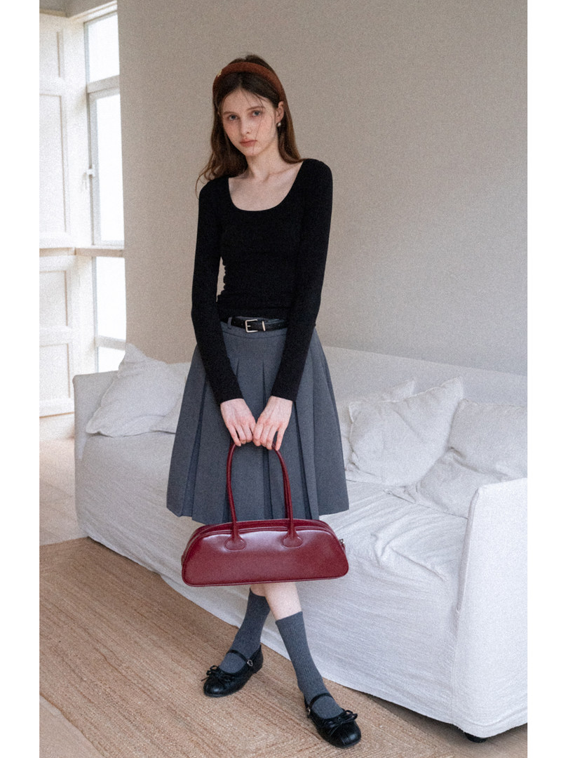 Woman wearing a black long-sleeve top and gray skirt while holding a burgundy handbag