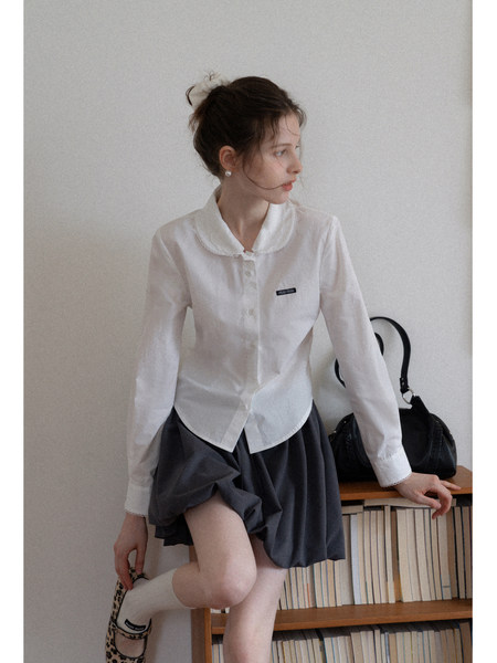 Woman wearing a white blouse and dark pleated skirt with black handbag