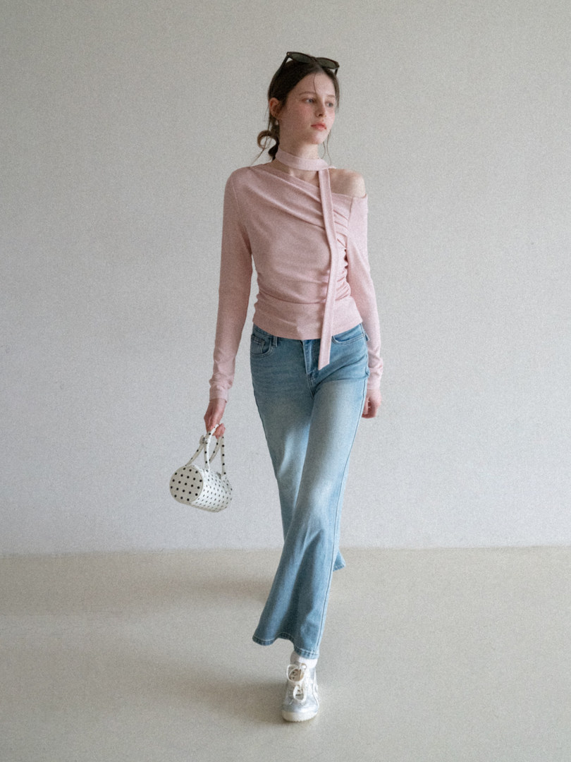 Model wearing a pink asymmetrical long-sleeve top with light blue jeans and a small polka-dot bag