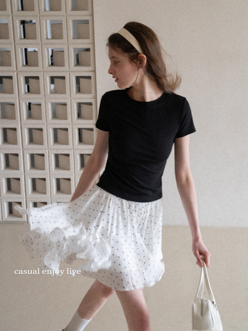 Woman wearing a black short-sleeve top and white polka-dot skirt with a small white handbag