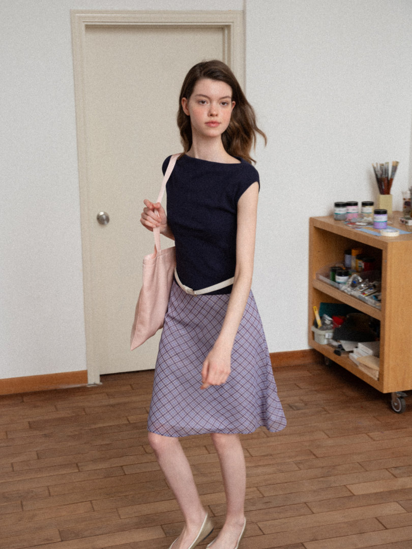 Model wearing a navy short-sleeve top with a plaid skirt and pink tote bag