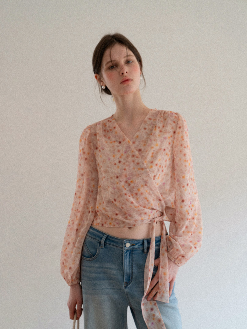 Model wearing a sheer floral wrap blouse with long sleeves and tie waist