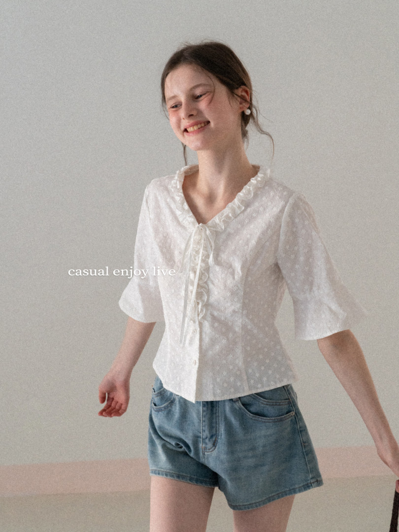Model wearing a white ruffled short-sleeve blouse with denim shorts